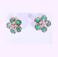Flower-shaped earrings with green gemstones and gold accents on a light background