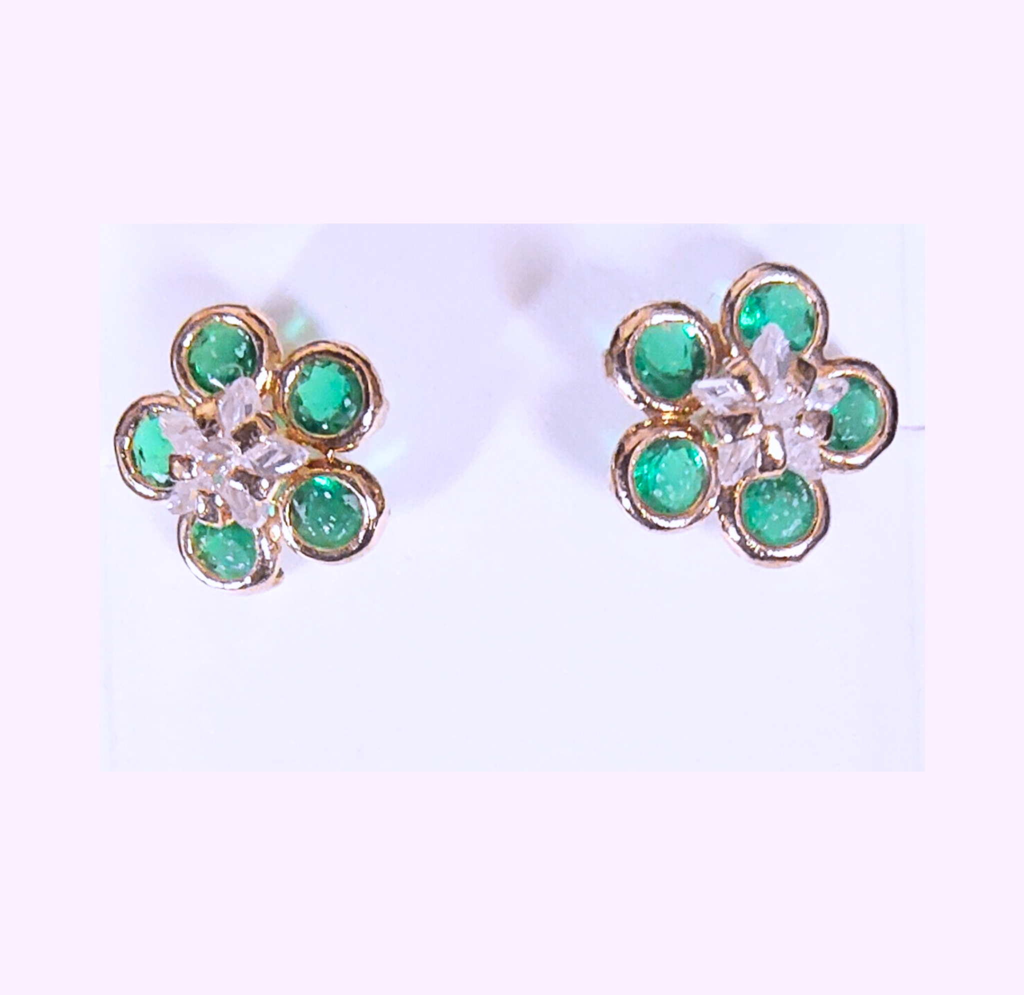 Flower-shaped earrings with green gemstones and gold accents on a light background
